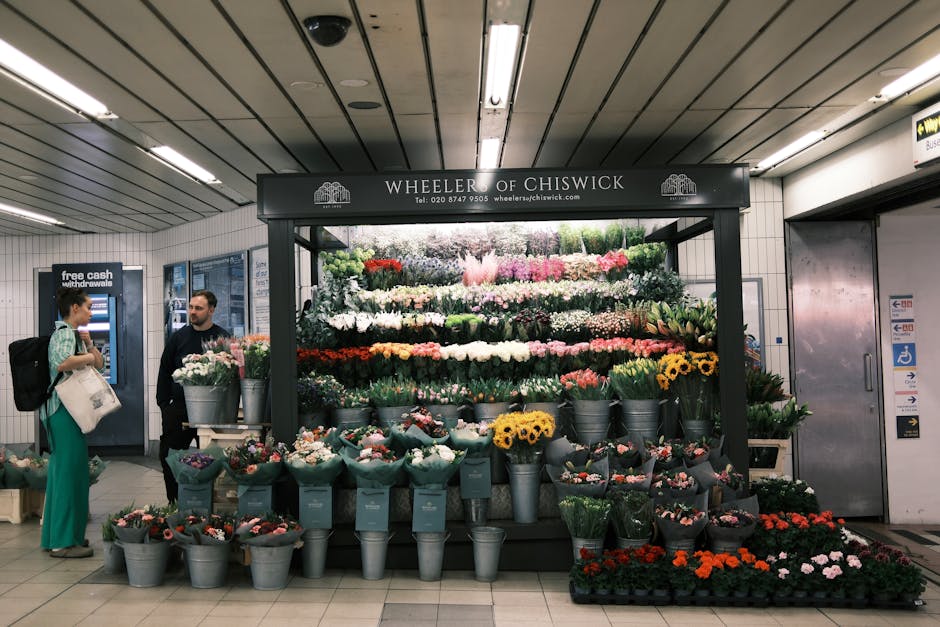 A flower stand inside Waterloo Station showcasing a variety of fresh floral arrangements, including bouquets of pink, white, yellow, and red flowers, arranged in metal buckets and wrapped with green t